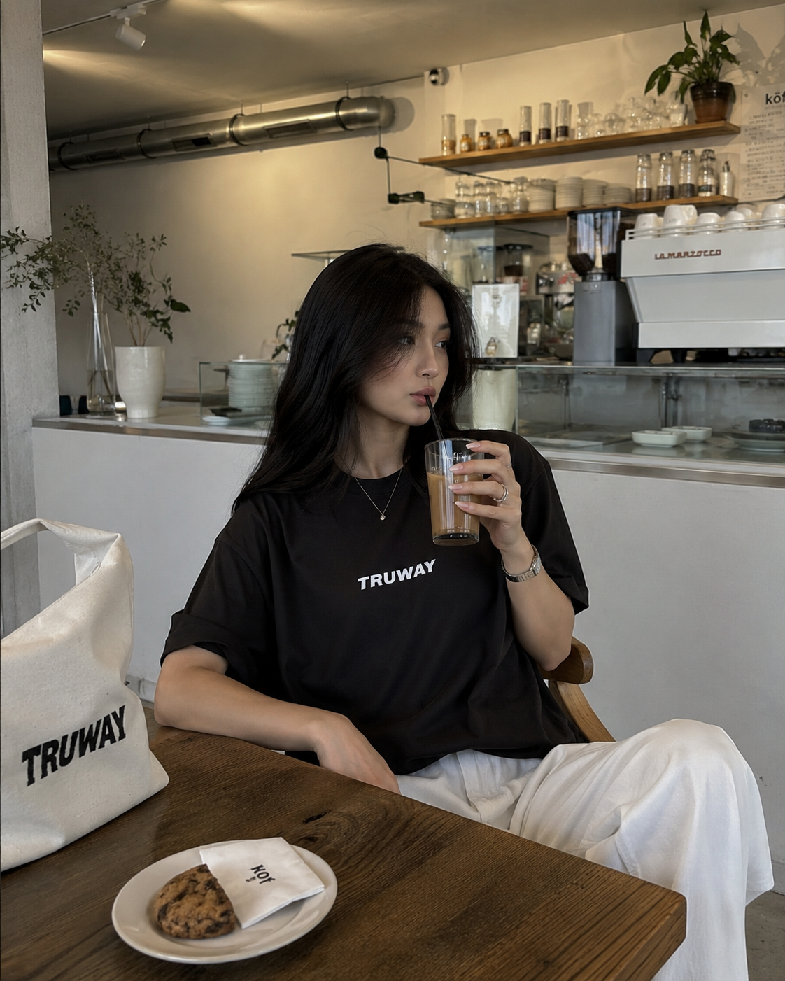 A woman in the black TRUWAY tee with a TRUWAY tote at a café